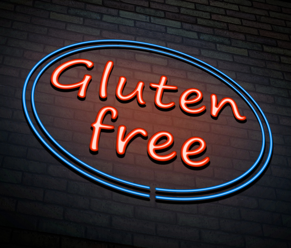 Neon sign with red lettering of "Gluten free" and surrounded by two neon blue circles all hung on a brick wall.