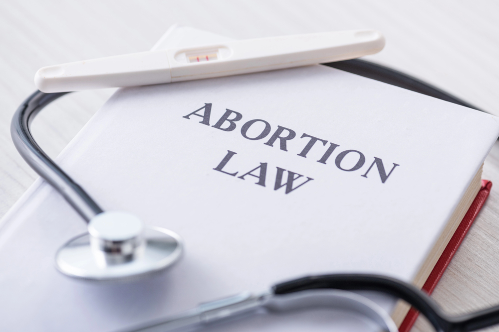 Abortion Law written on a notebook with a stethoscope and a pregnancy test draped on top of the notebook